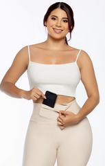 Woman wearing a white top and beige pants holding a phone on a plain background